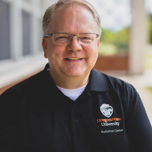 A person wearing a dark colored shirt smiles at the camera. 